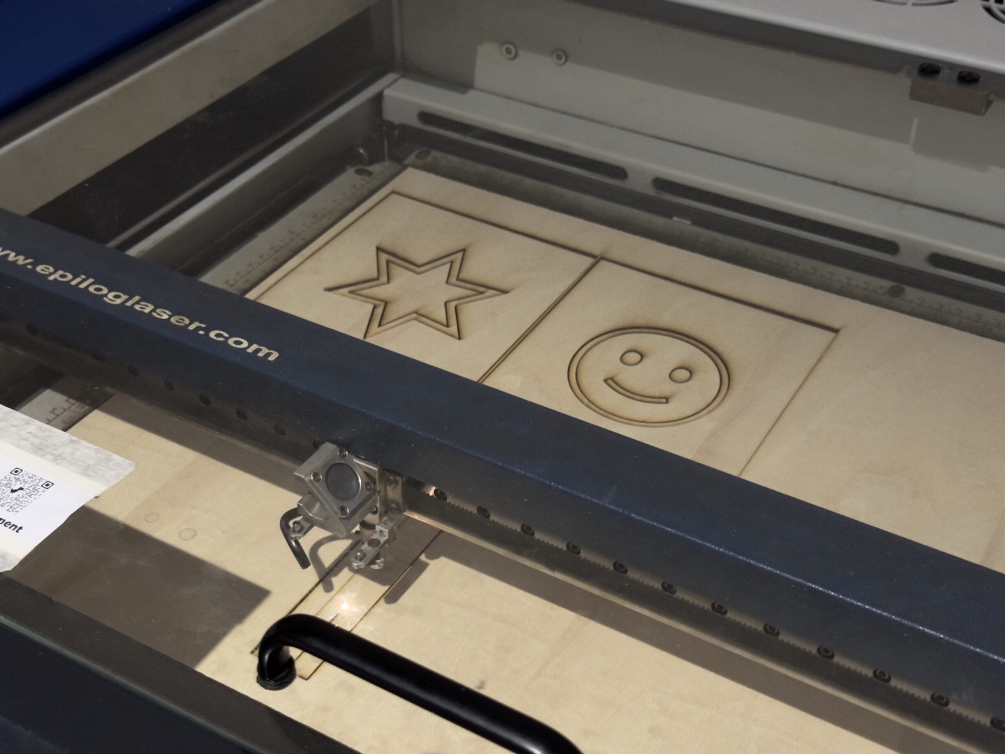 Laser cutter engraving the star and smile shadow panels in plywood