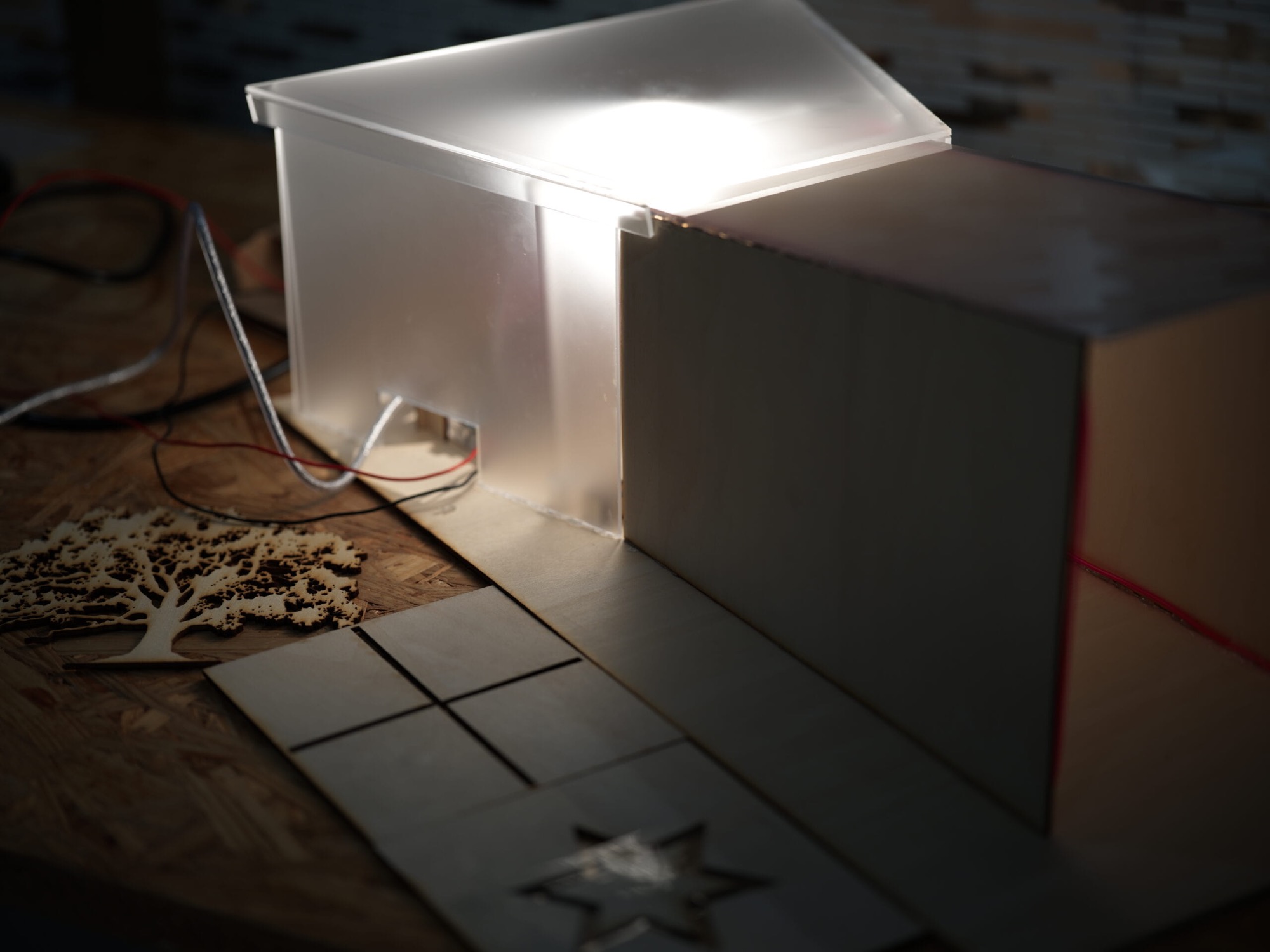 Exterior of the model with a frosted acrylic volume glowing under a halogen source, tree and star panels laid out beside it