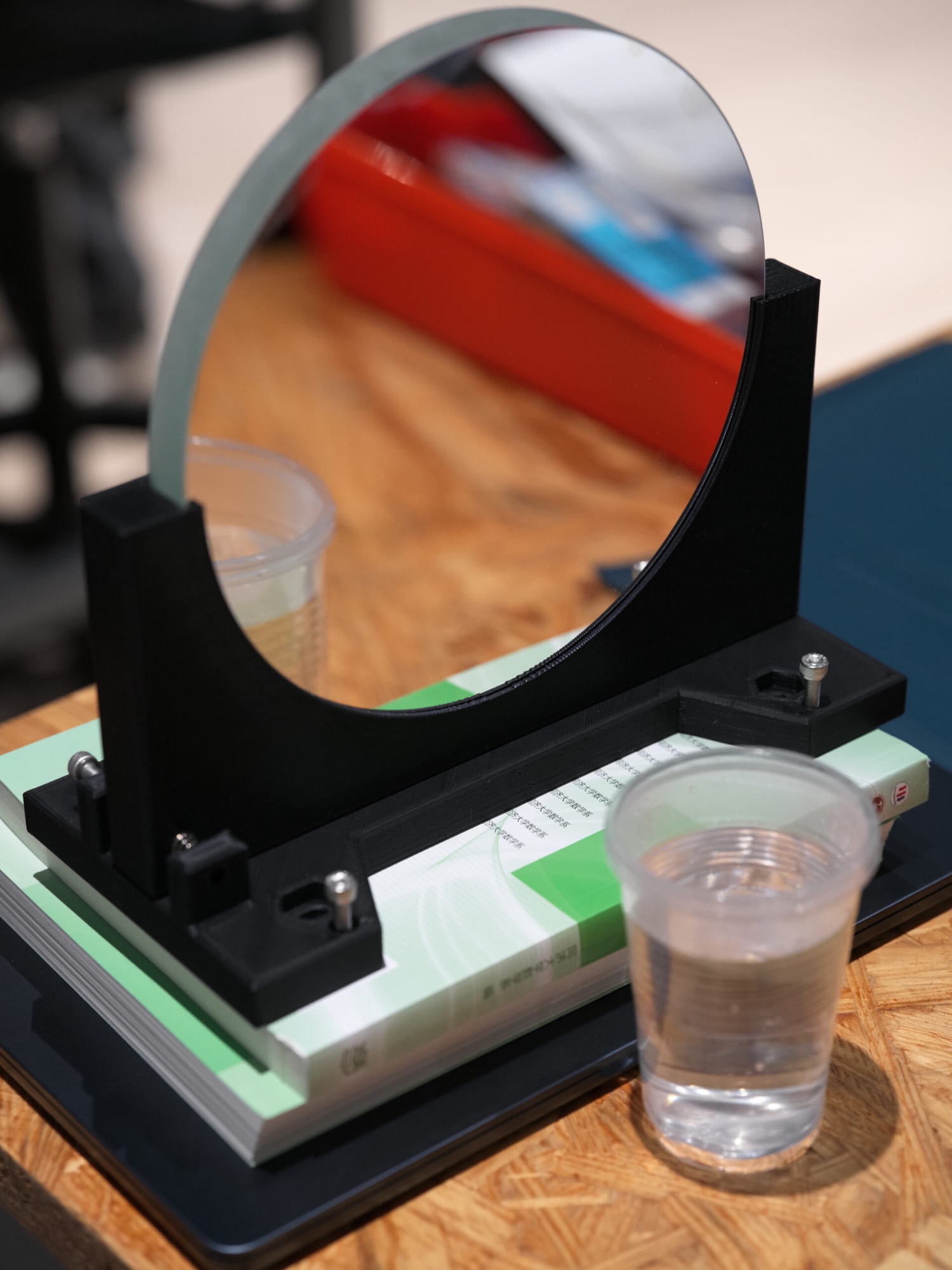 Concave mirror held upright by a black 3D-printed shelf on a workbench