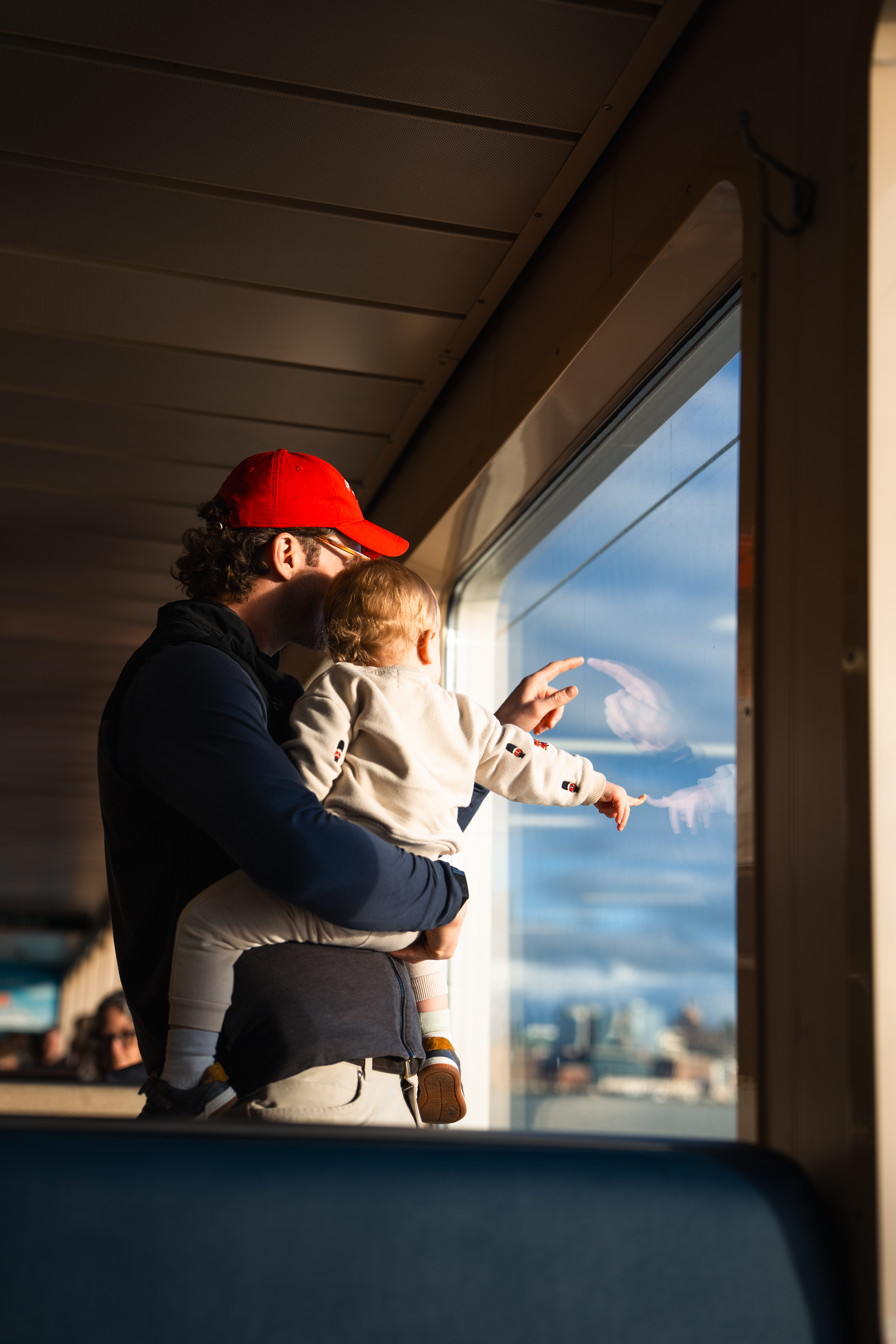 Father holding son, both pointing out ferry window