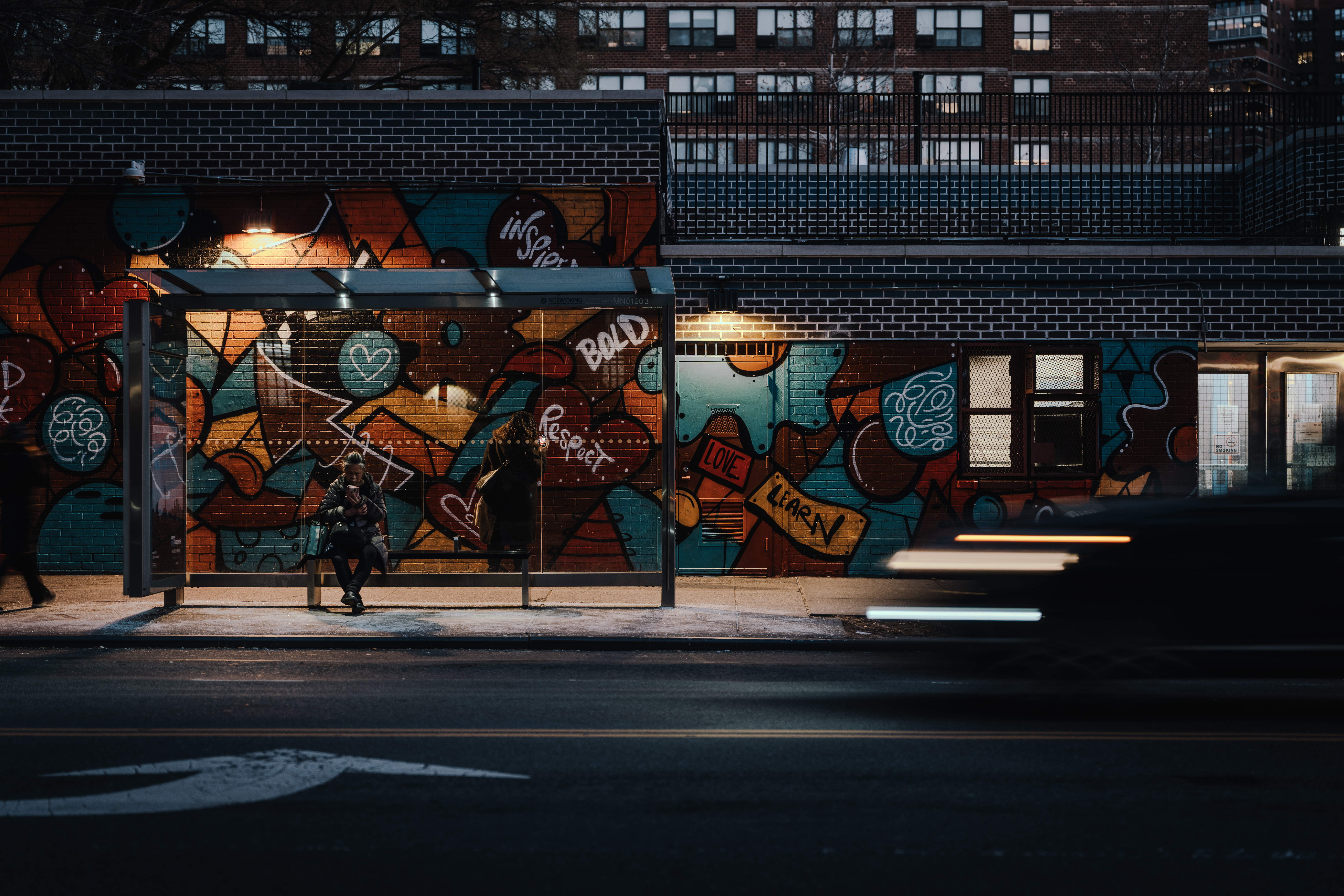 Elderly woman at bus stop in front of graffiti wall