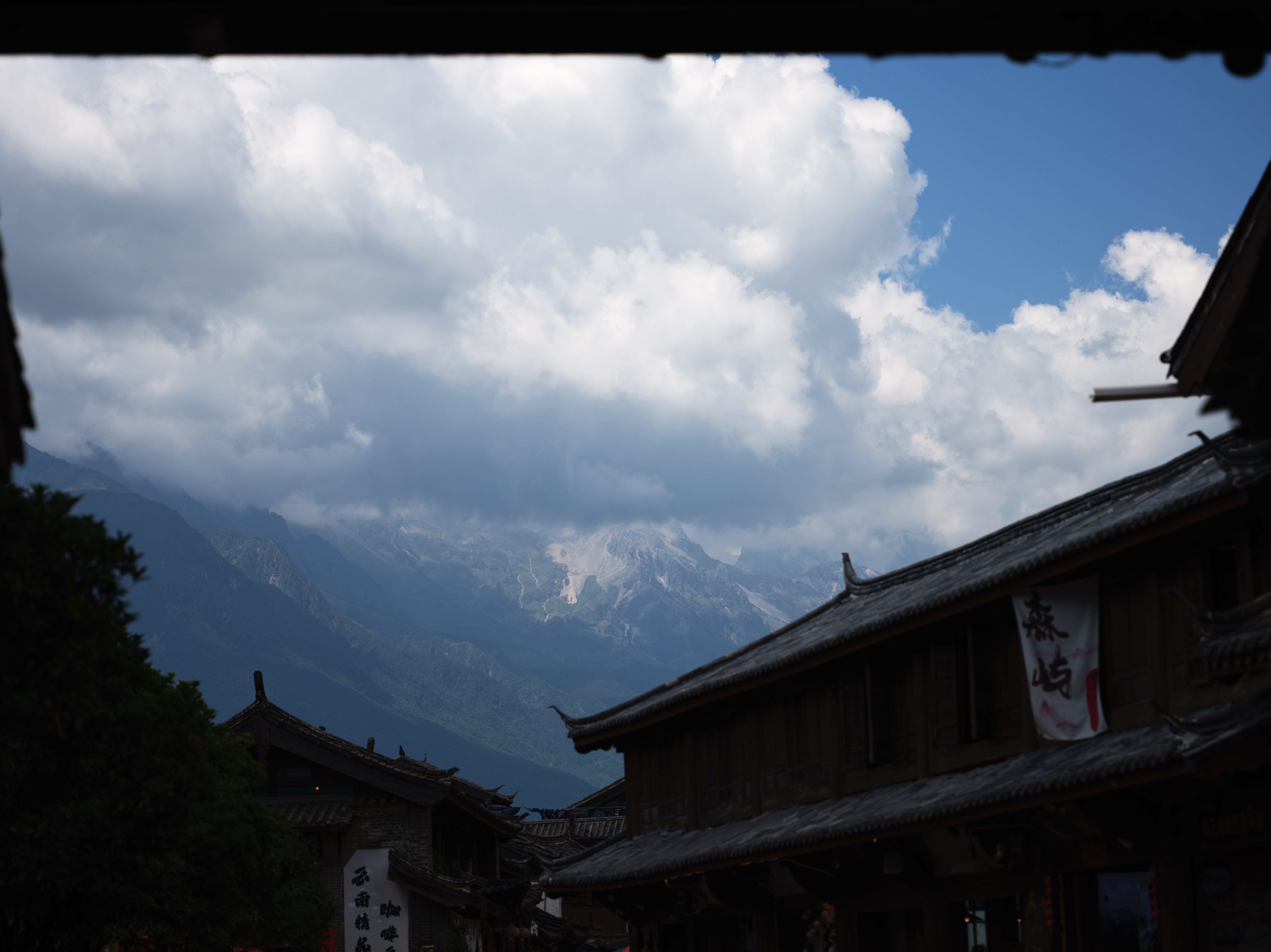 Yulong Snow Mountain peak emerging from clouds framed by traditional eaves