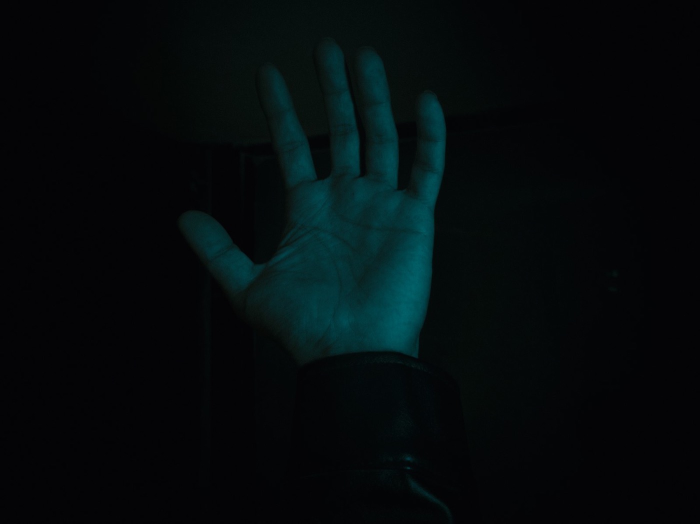 An open palm raised in the dark, lit by the cool glow of a screen
